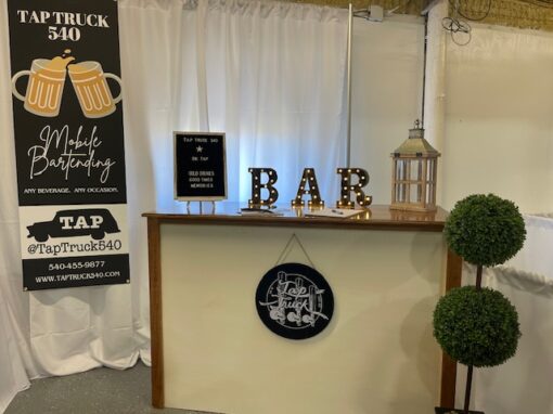Bridal showcase bar setup with a Tap Truck 540 banner, lit BAR letters, a small tree, lantern, and a sign promoting mobile bartending services.