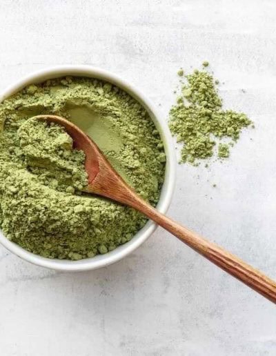 A bowl filled with green powder and a wooden spoon, with some powder spilled on a light-colored surface.